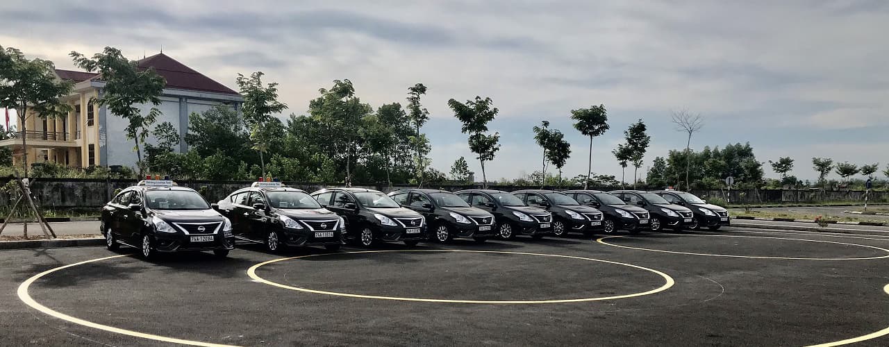 Hàng xe sedan đen xếp trên sân tập có vạch kẻ.